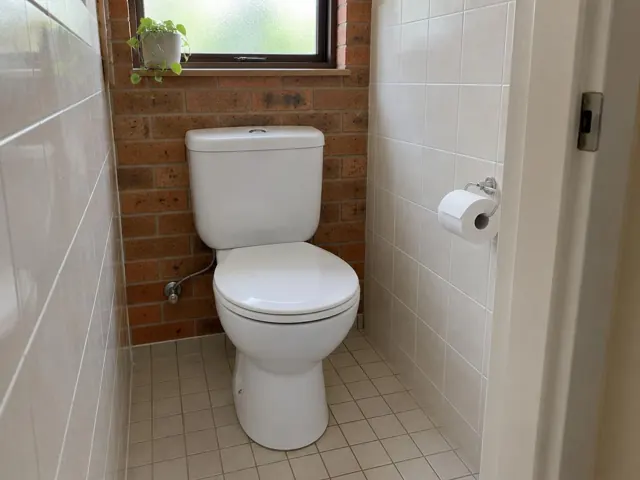 Clean white toilet in a small tiled bathroom with brick wall and window in Narrabeen