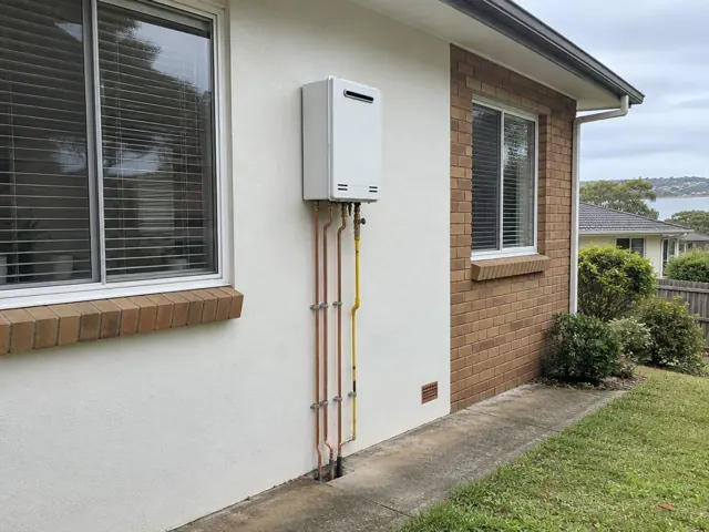 Wall-mounted hot water unit with exposed copper and gas pipes on an exterior brick and rendered wall in Cromer